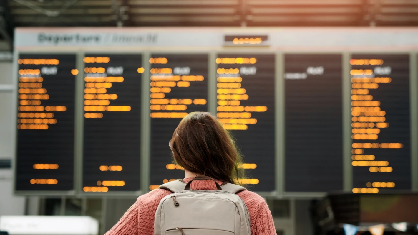 A woman with a backpack looks up at a departures board