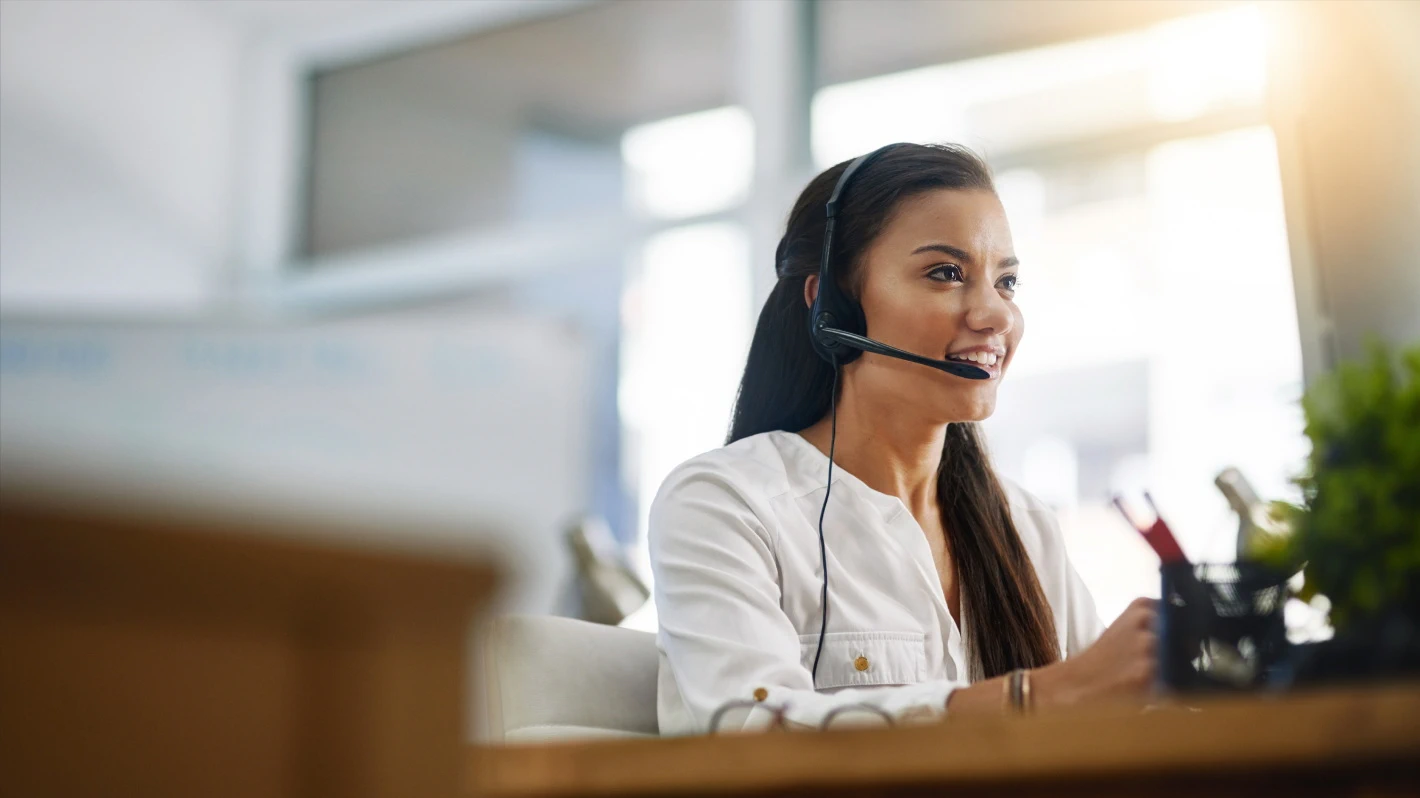 A friendly female customer service representative with dark hair, wearing a headset and a white shirt