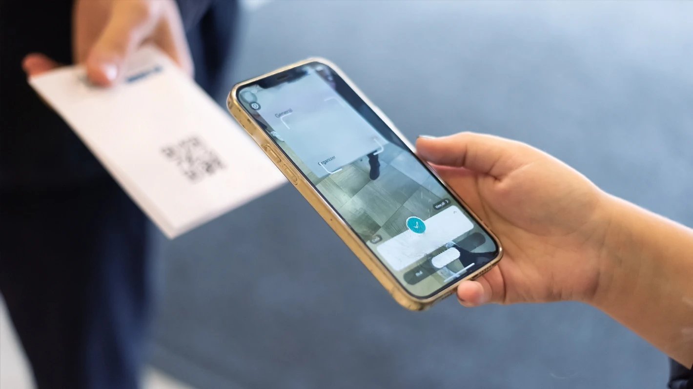 A person scans a QR code with a smartphone, which is on a white piece of paper