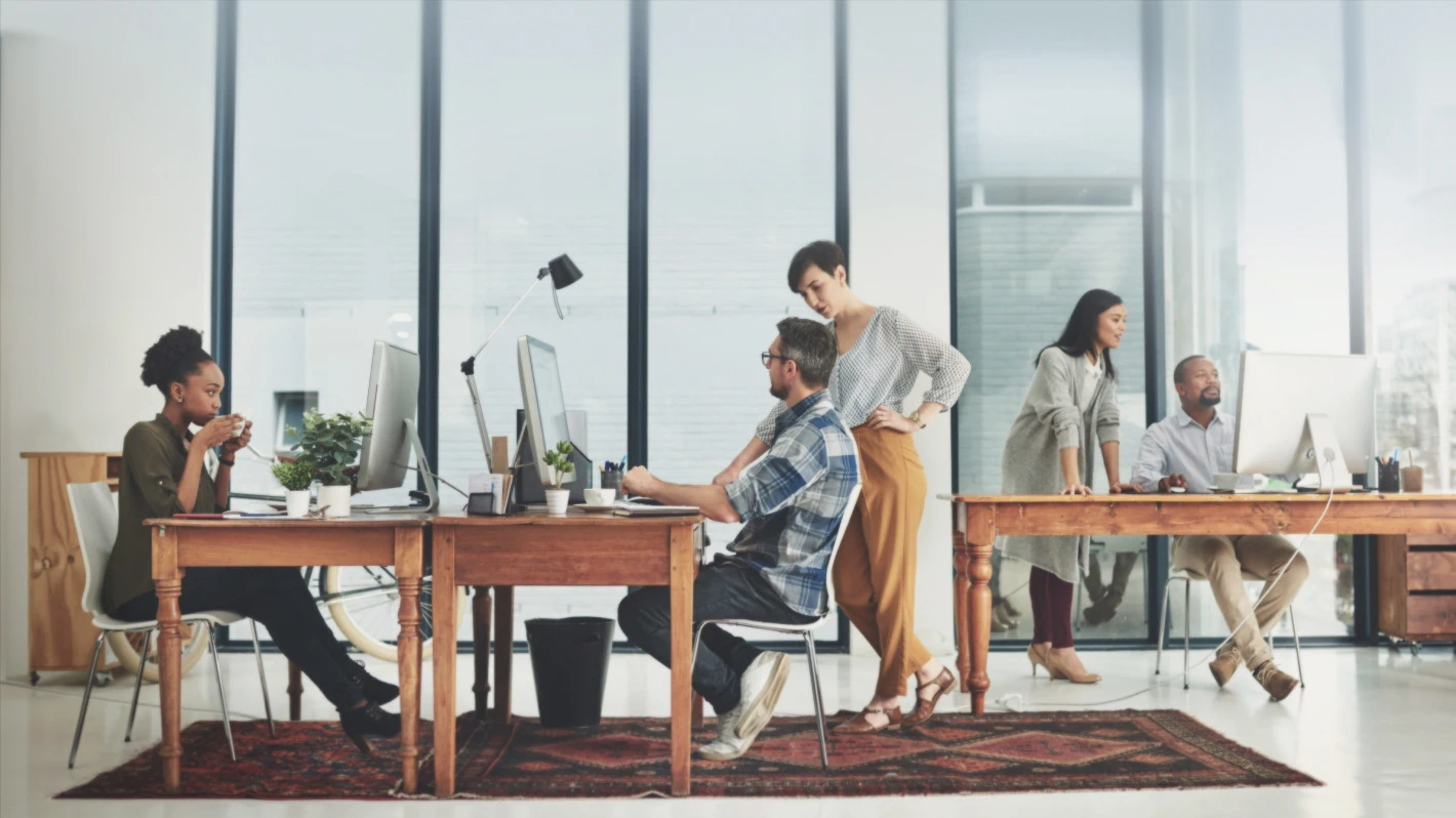 A group of professionals working in a modern office space, some at desks with computers and one drinking a beverage