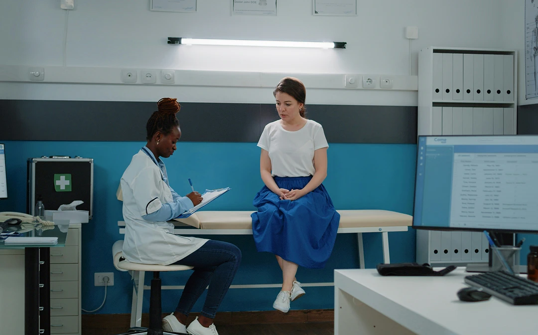 Female doctor taking notes while consulting a patient in a medical clinic examination room