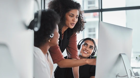 A team of women wearing headsets reviewing a computer screen while providing customer support