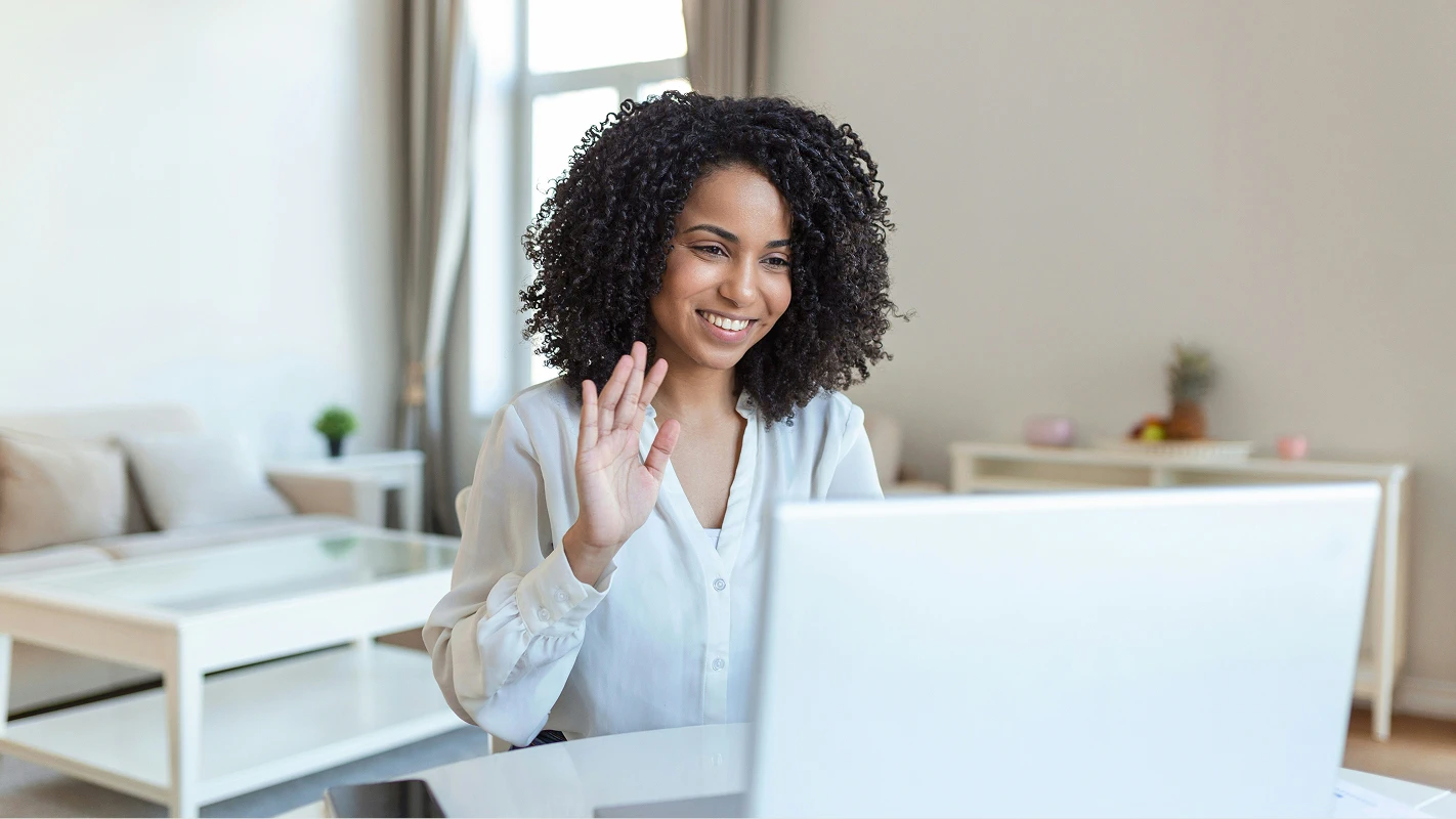 Smiling woman with curly hair waving during a video conference.
