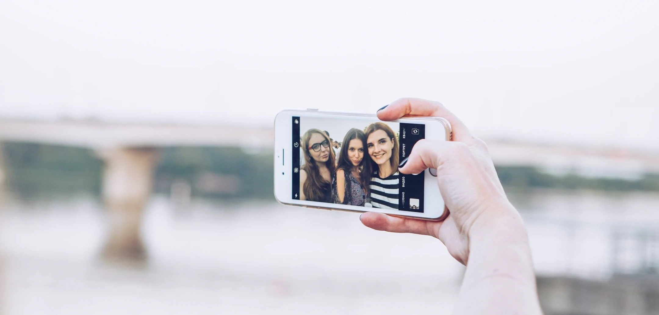 Close-up of hand holding smartphone taking a selfie of three happy women