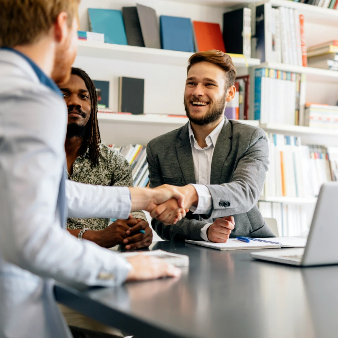 Three men in business suits having a meeting around a table, two of them shaking hands