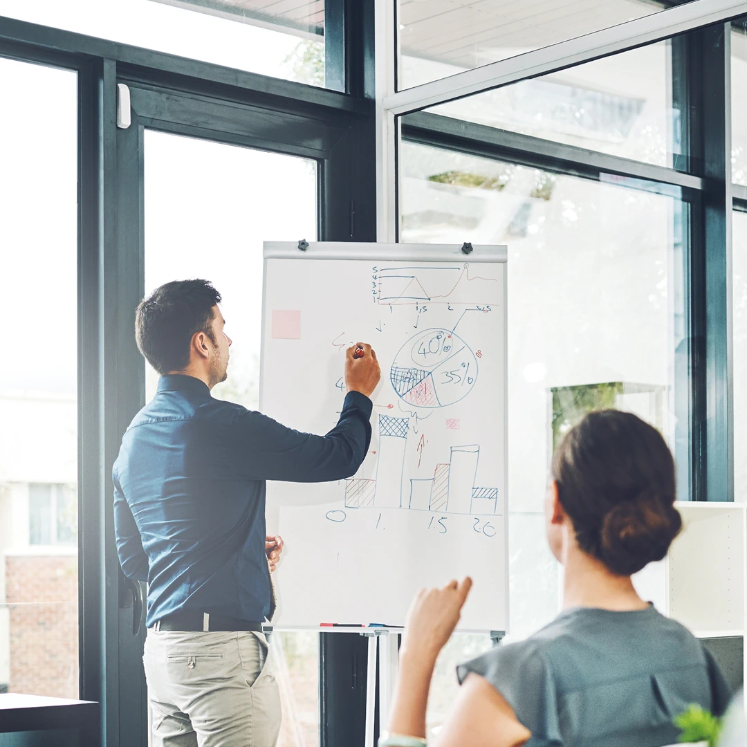 Man presenting business data using a whiteboard with charts and graphs in front of a woman