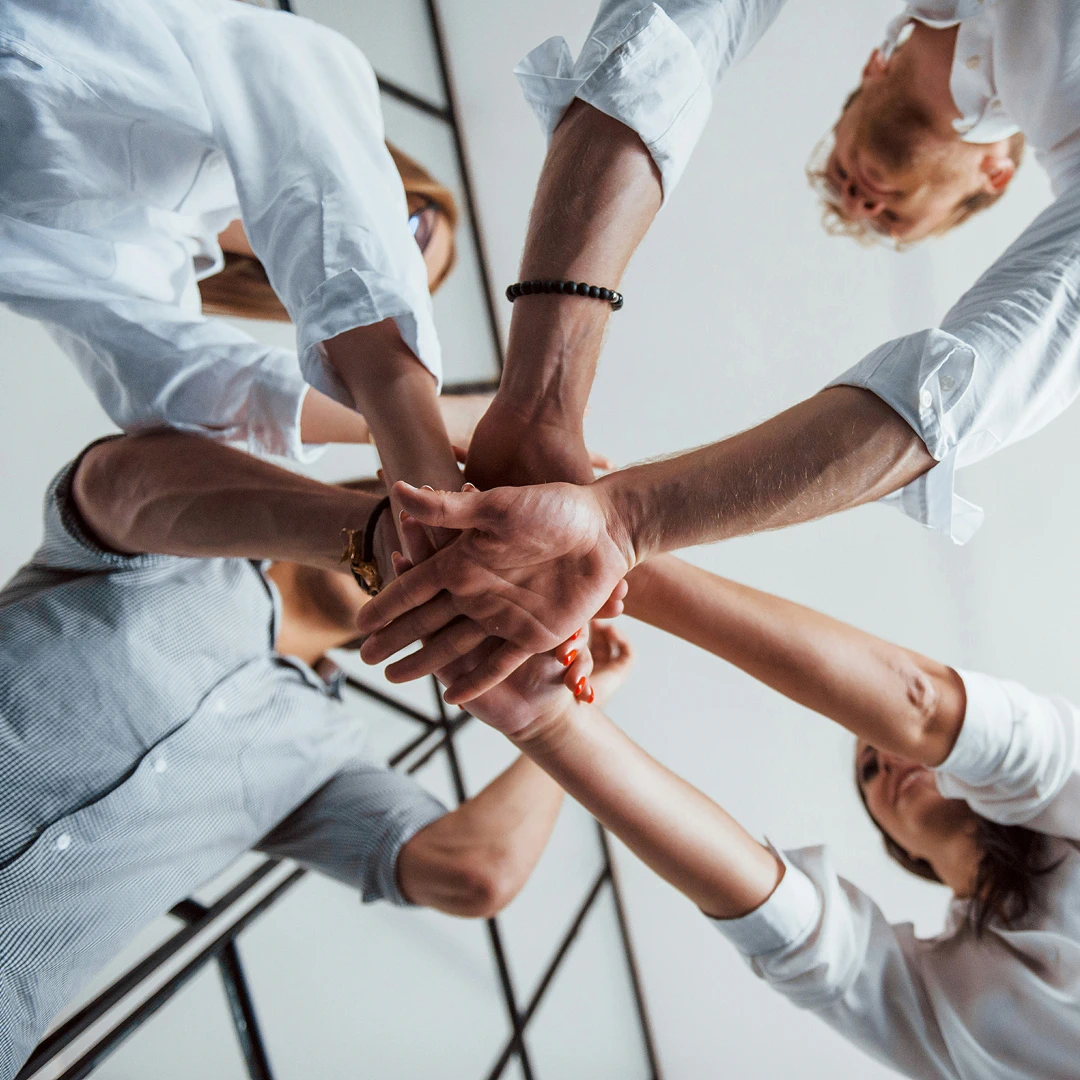 Several people in white shirts joining their hands together to show teamwork