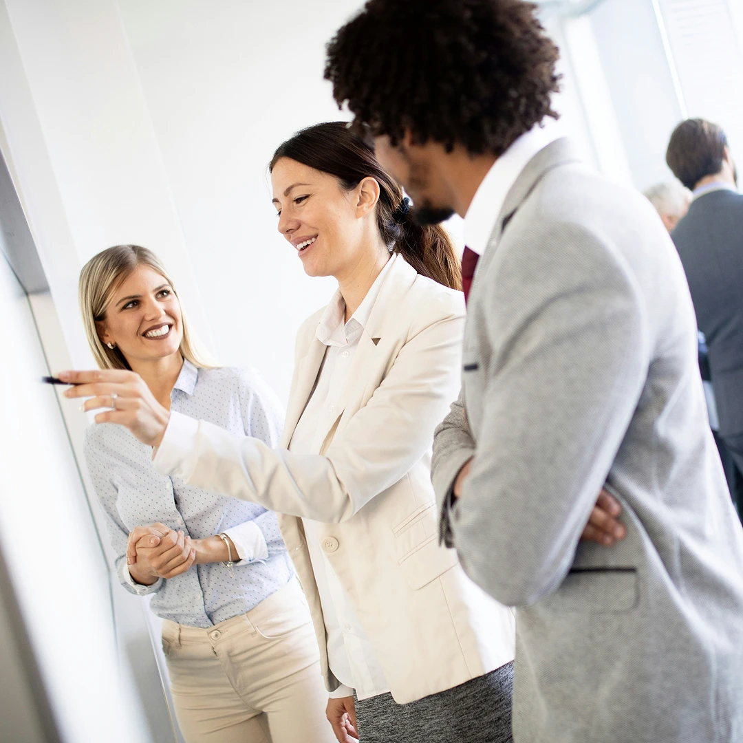 Group of three business professionals looking at a whiteboard and discussing ideas