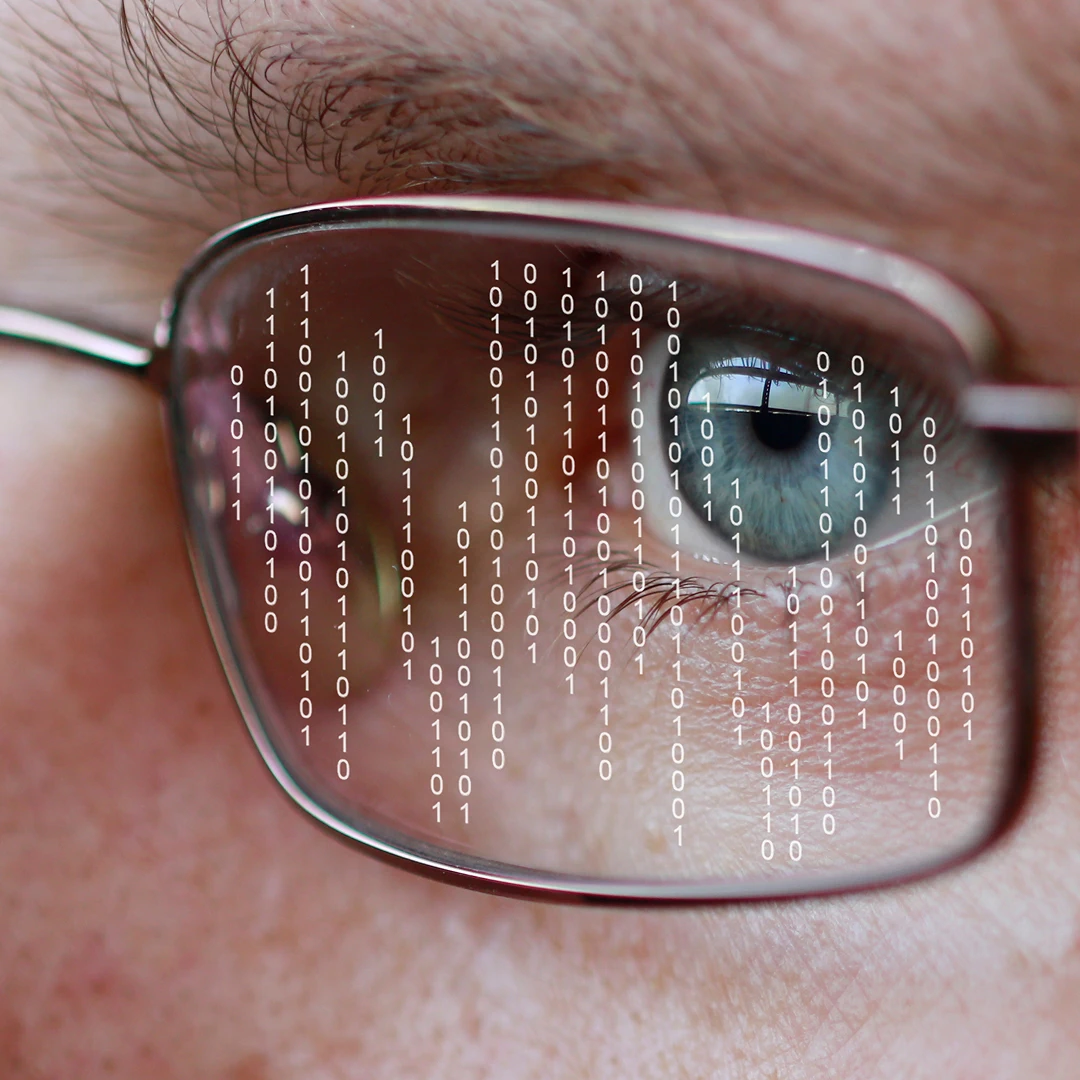 Close-up of a man's eye behind glasses, displaying binary code