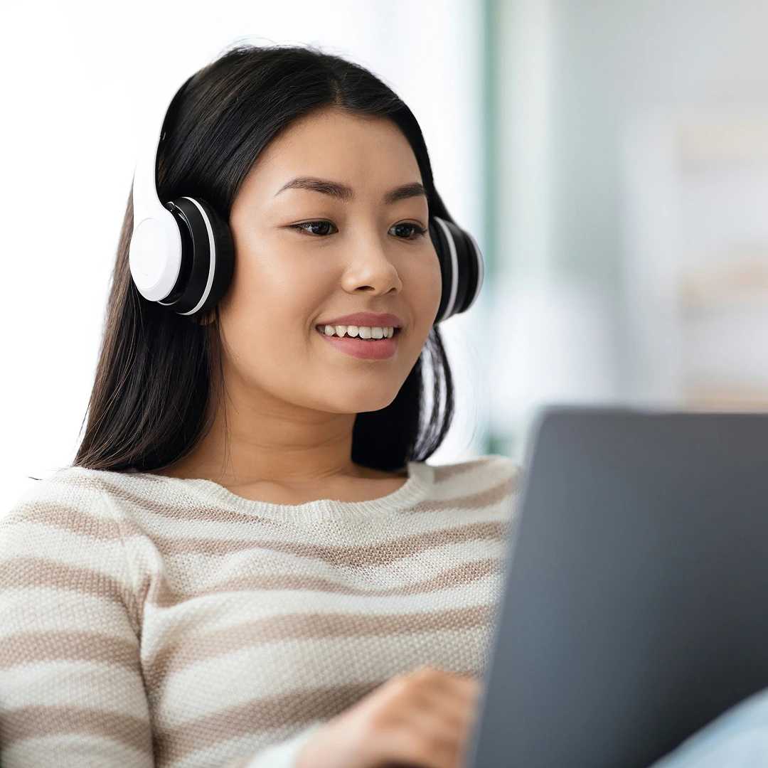 A female retail customer support specialist with black hair, wearing a soft striped sweater and black headphones, working at her laptop