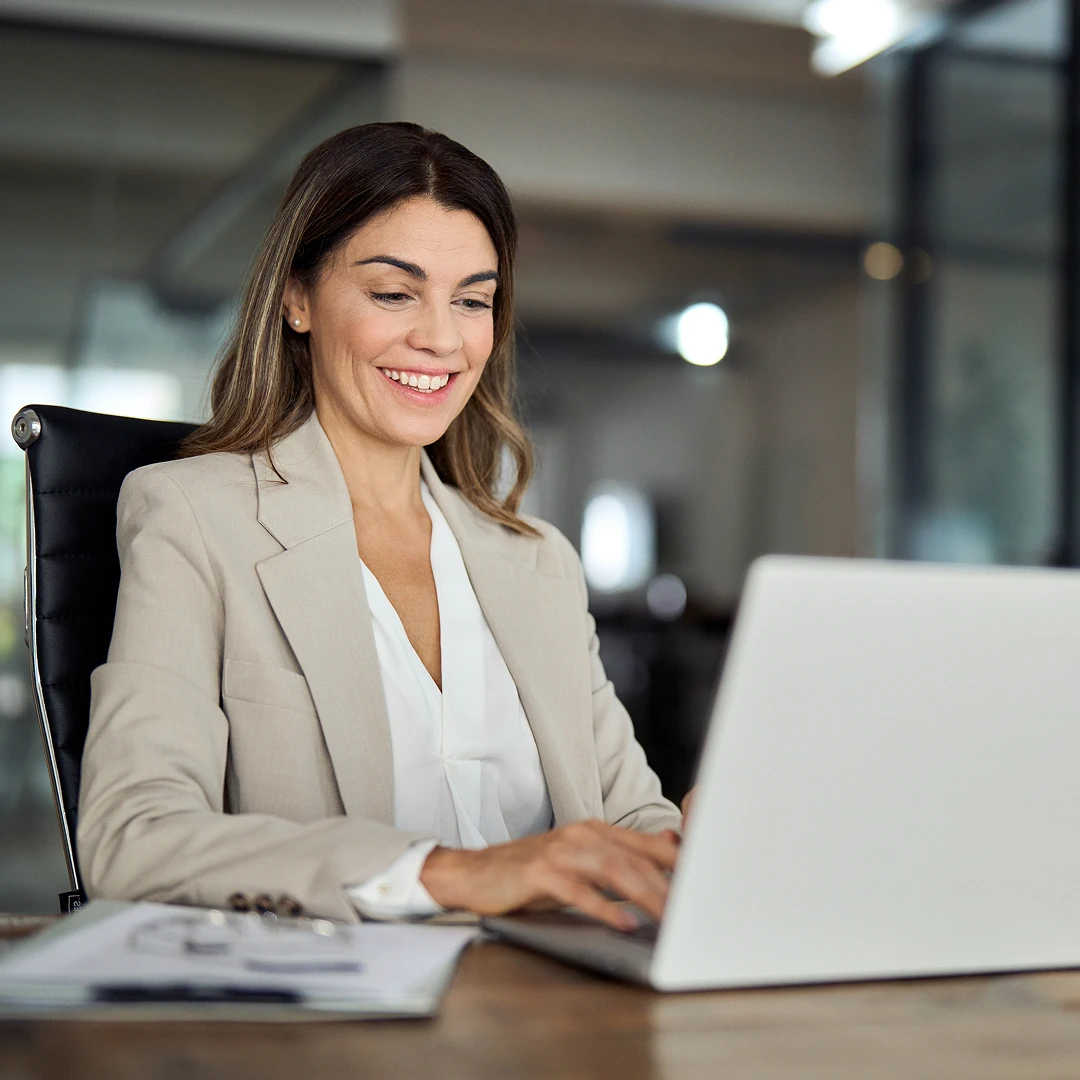 Smiling woman in a blazer working on a laptop in a modern Polish call center.