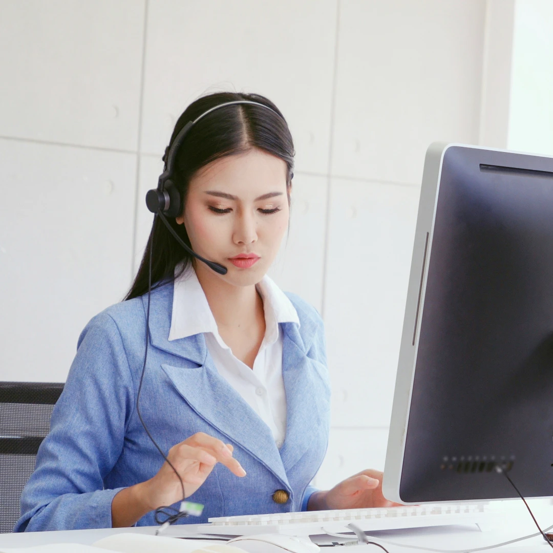 Female customer support representative wearing a blue blazer and a headset, focused while working at a computer