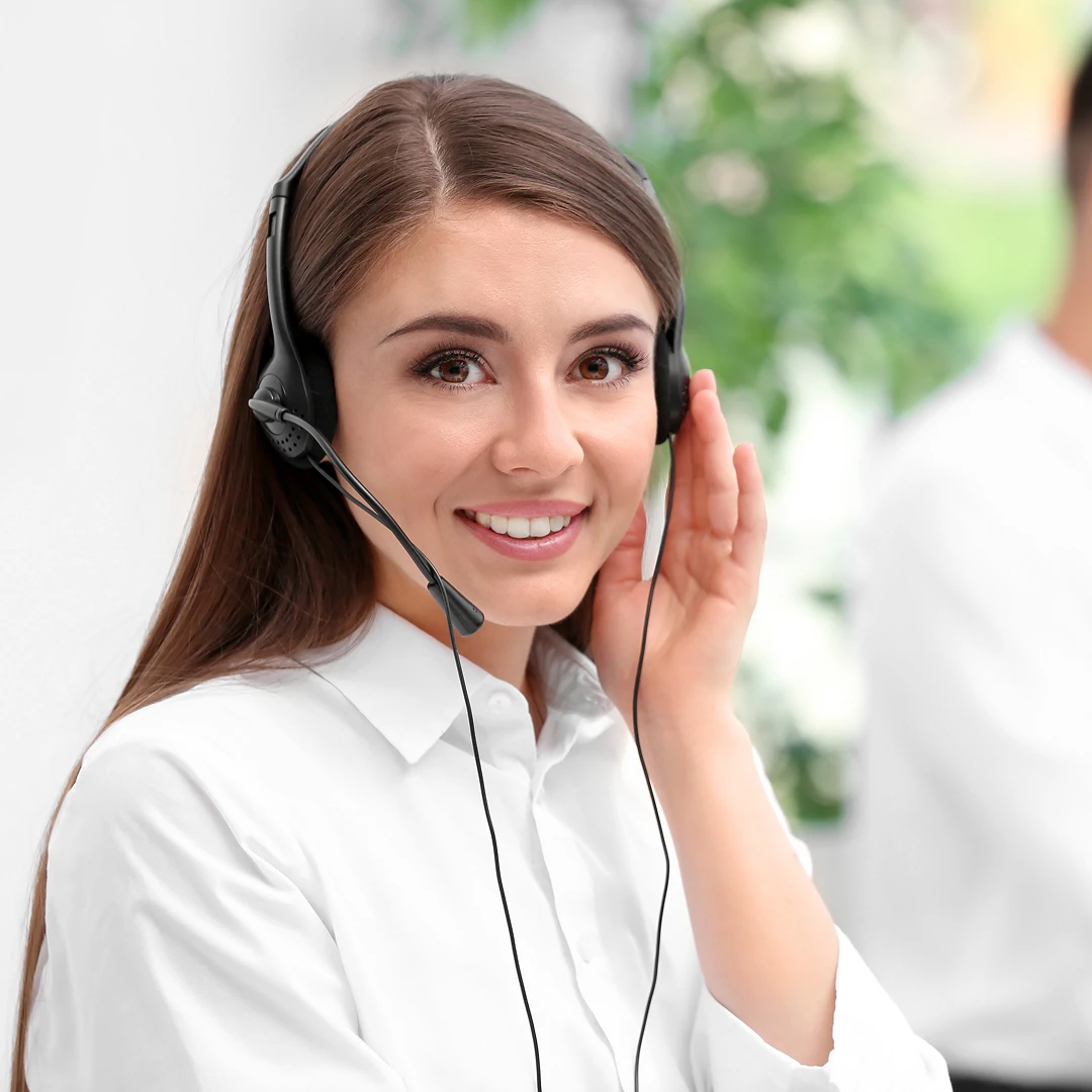 Smiling female customer support agent with long brown hair and headset in a modern call center