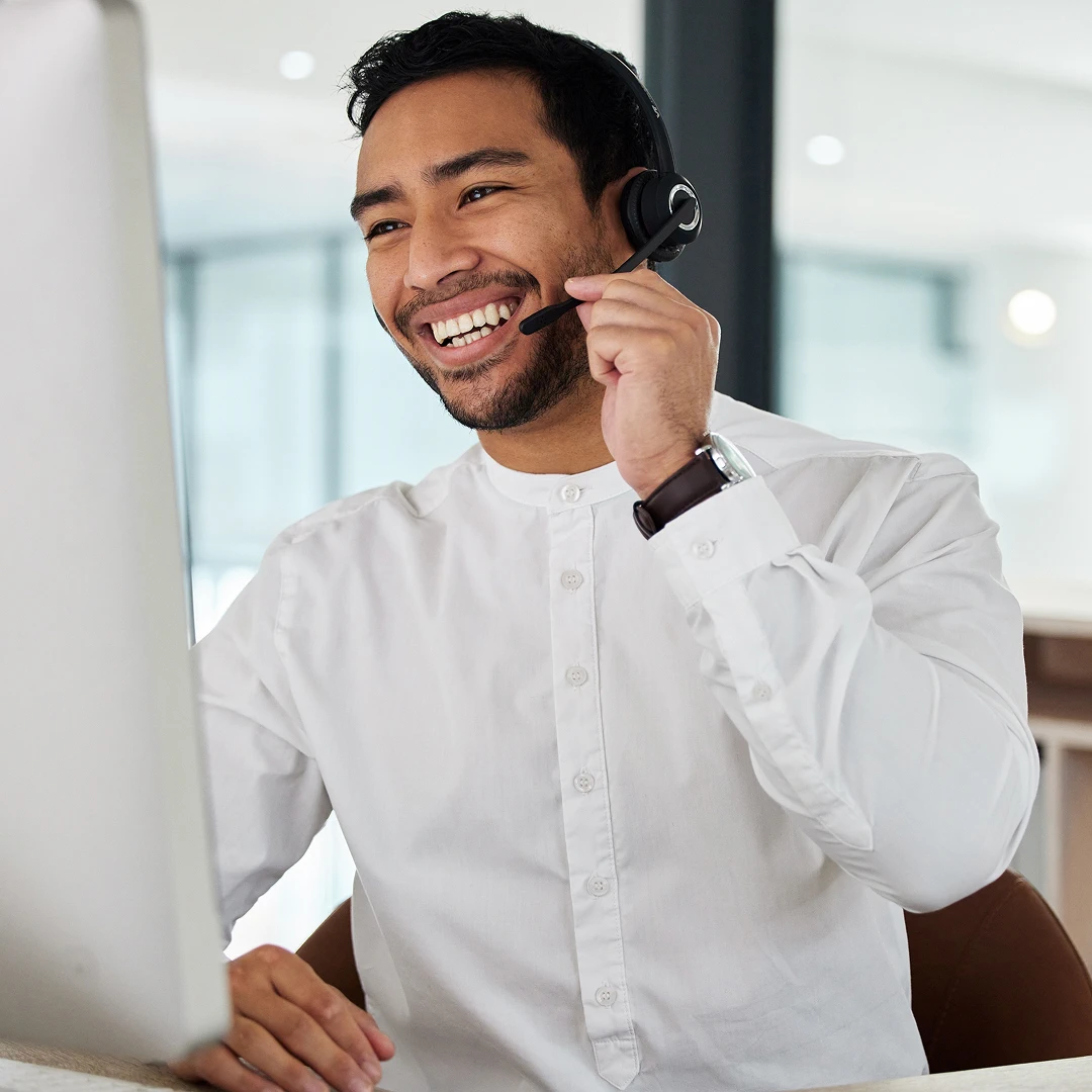 Smiling customer support agent with short black hair, wearing a headset and white shirt, providing client assistance