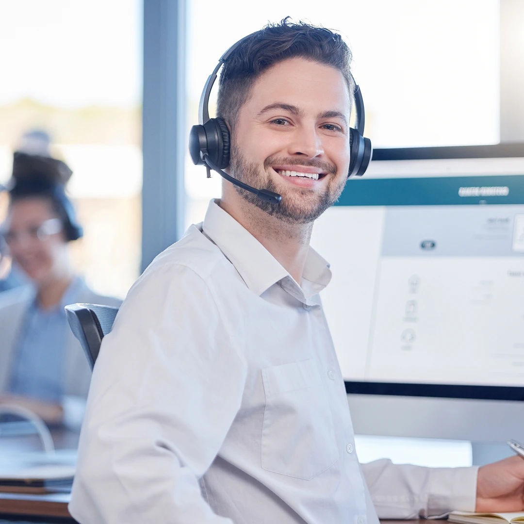 Smiling customer support agent with short brown hair and a beard, wearing a black headset and a white dress shirt