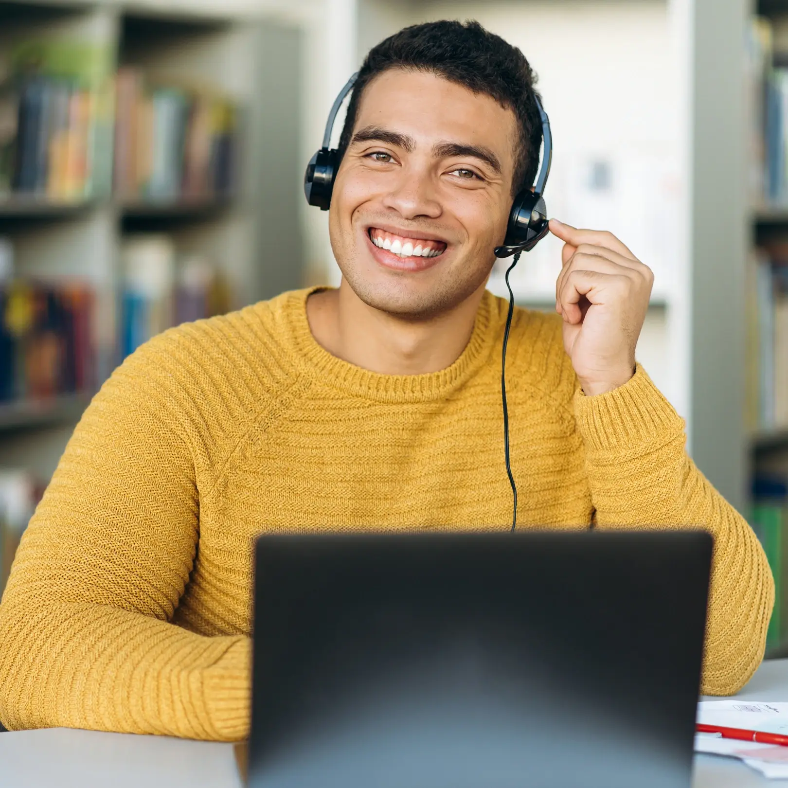 Smiling male customer support agent with short black hair, wearing a headset and a yellow sweater