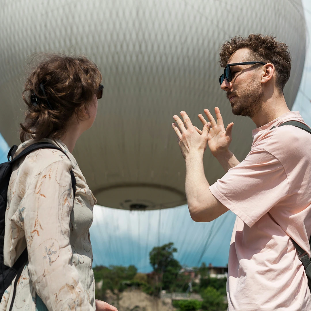 Man gesturing while talking to a woman, with a large white shape behind them