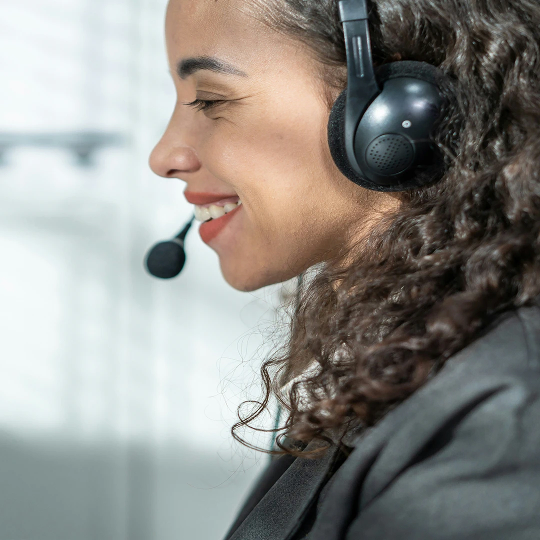 Smiling customer support agent with wavy hair and a headset, wearing a grey suit