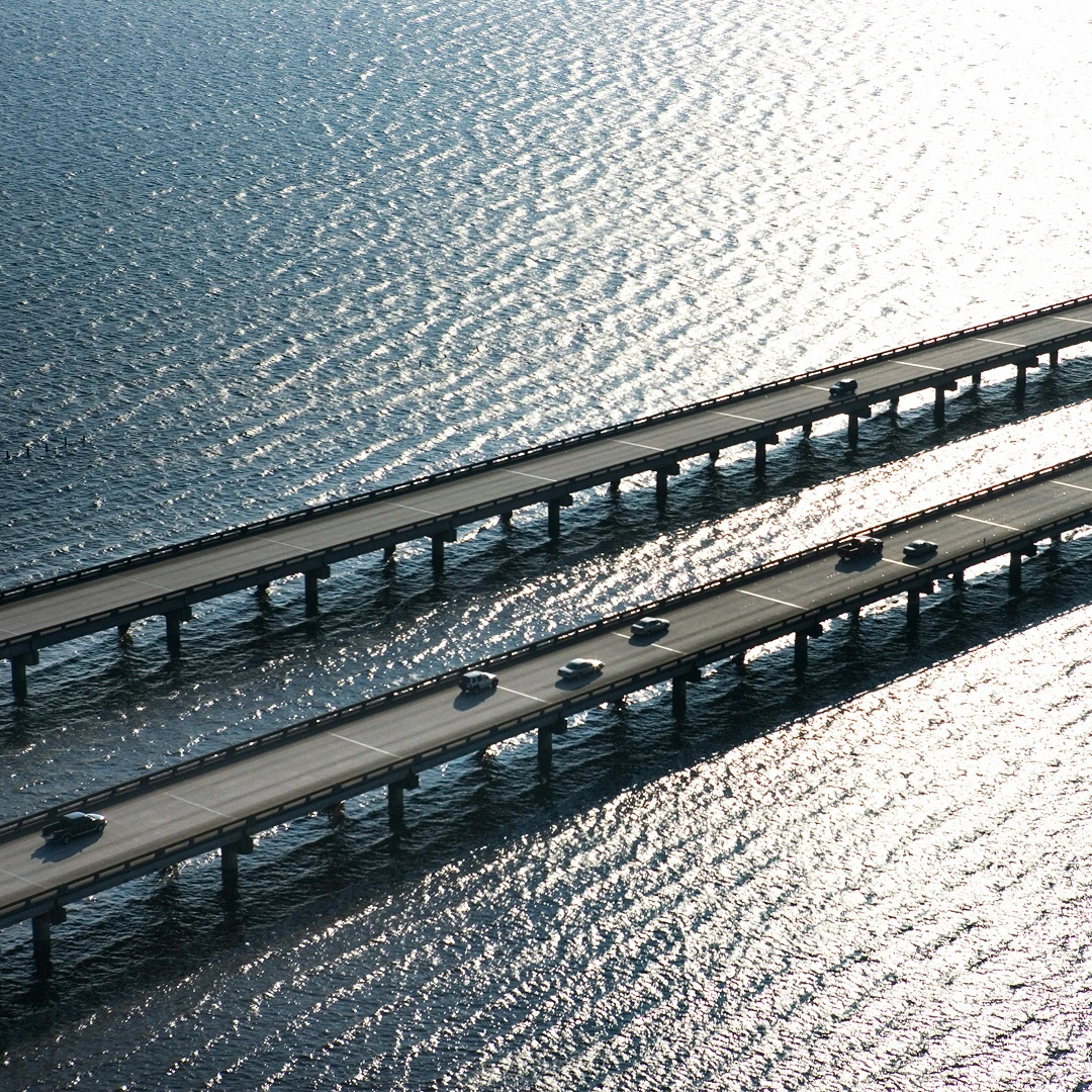Two long bridges extending across rippling water that reflects sunlight