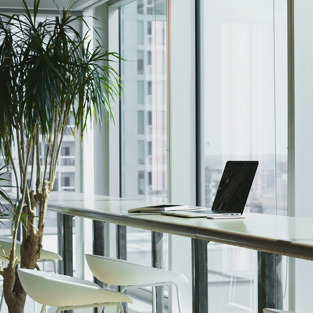 Modern workspace with a laptop, notebook, and plant near a large window overlooking a city