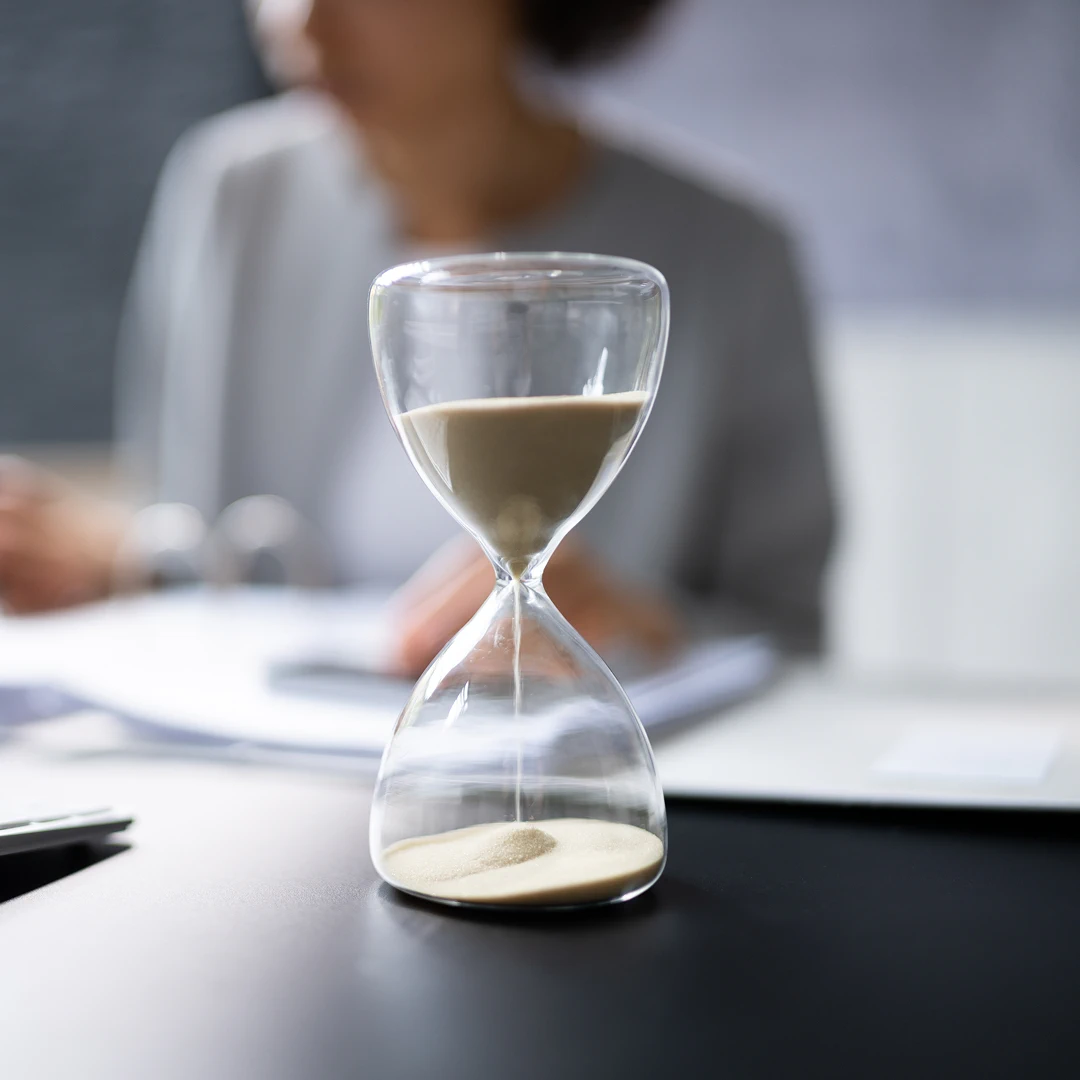 Hourglass on a desk with a person working in the background
