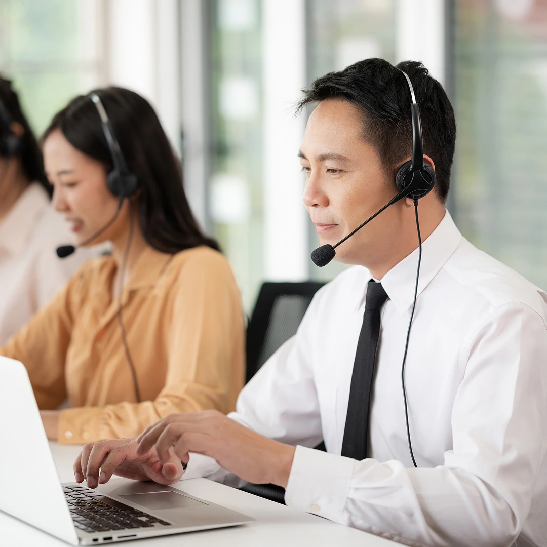 Focused customer support agent wearing a white shirt and headset, working at his own workstation