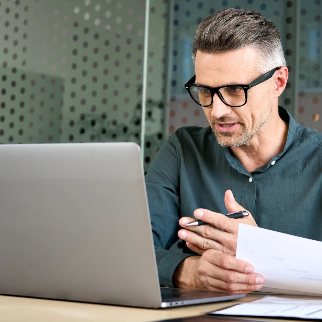A man in a green shirt and glasses is communicating via video call in a modern office