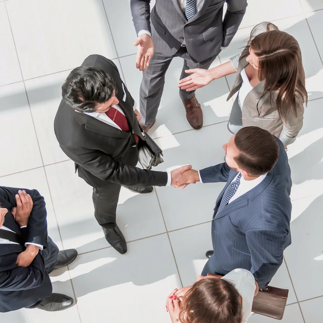 Two men in suits are shaking hands while other colleagues look on
