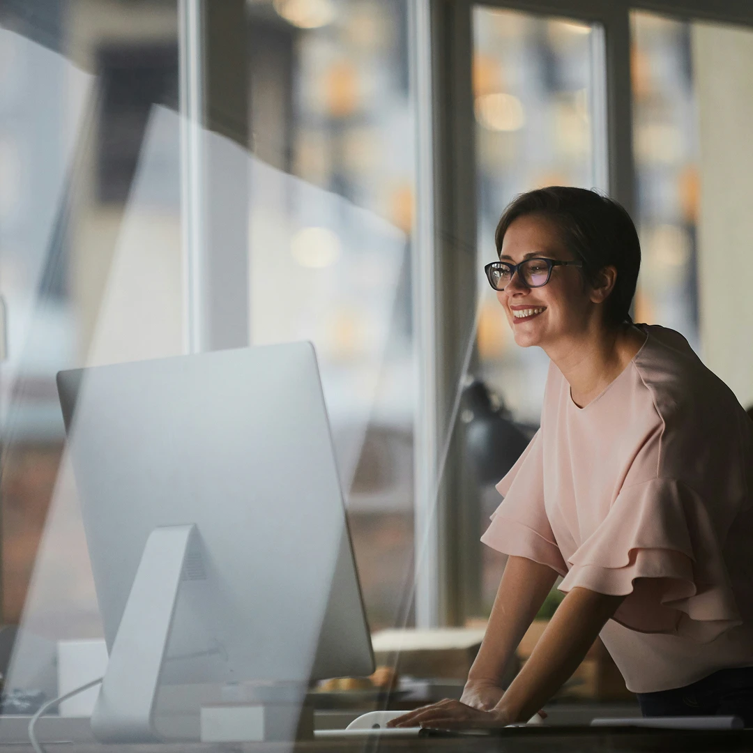 Ecommerce customer support representative with short dark hair and glasses, smiling while looking at a computer screen in an office setting