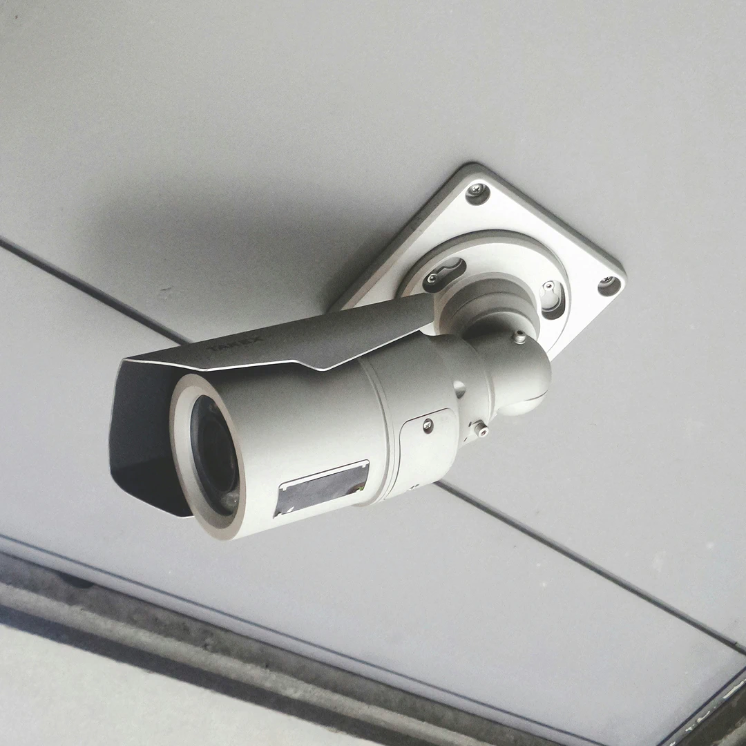 Close-up of a gray security camera, mounted on a white ceiling
