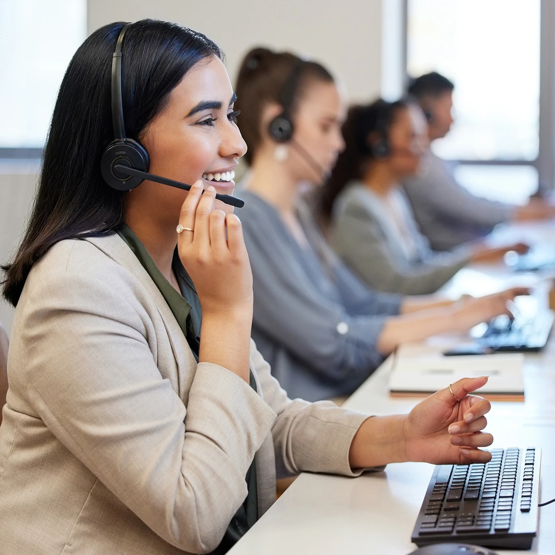 A team of smiling customer support representatives wearing headsets, working at their computers in a call center office in Los Angeles