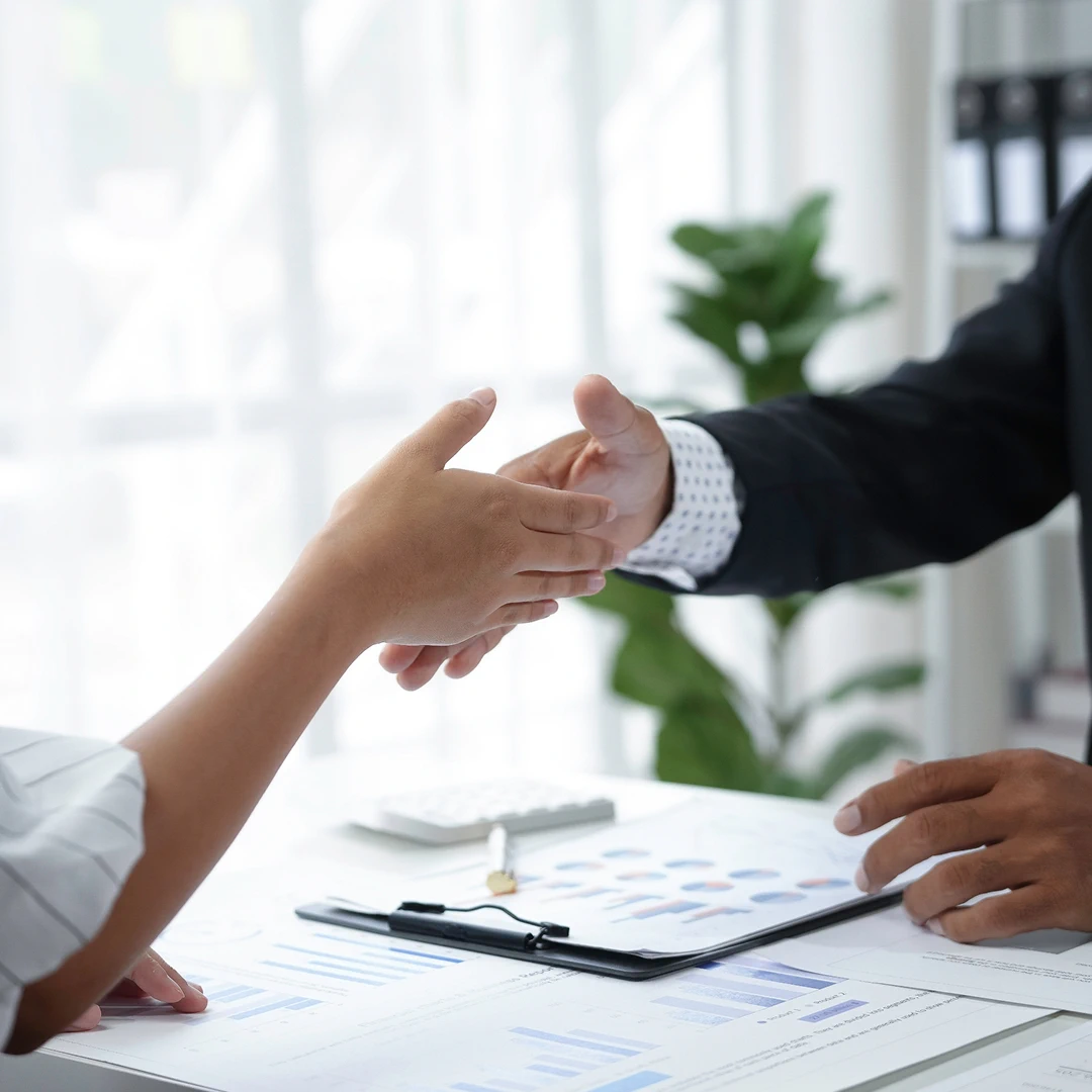 Close-up of two people shaking hands across a desk covered with charts and graphs