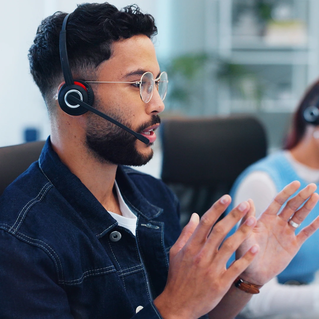 Concentrated customer support agent wearing a denim jacket, glasses, and a headset in a modern New York call center office