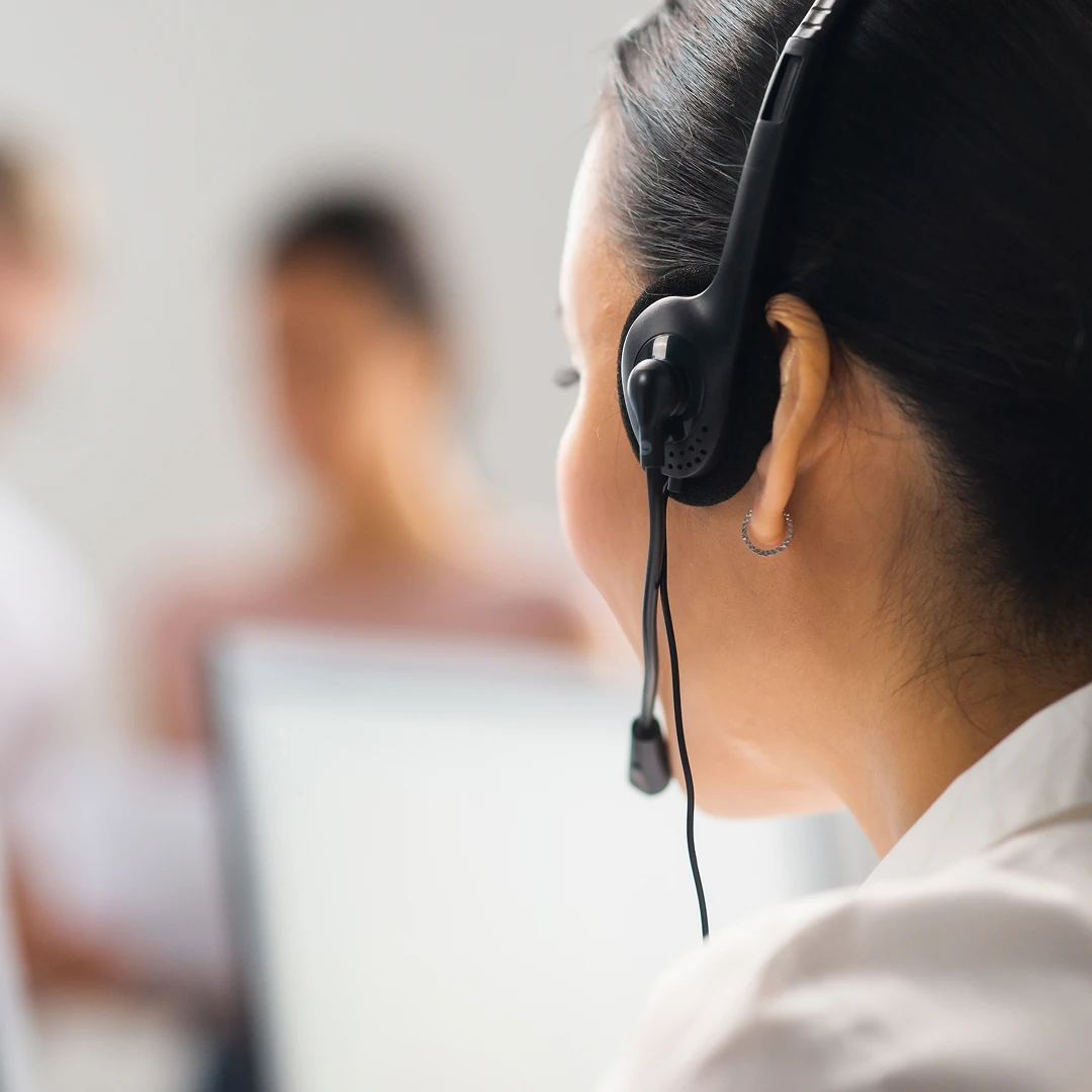 Close-up of a female customer support agent wearing a headset and a white blouse, viewed from behind
