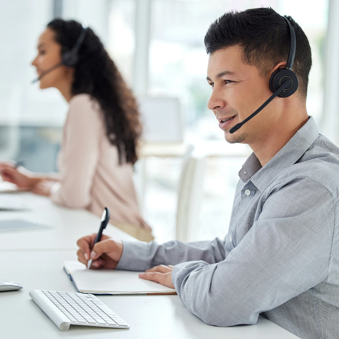 Attentive customer support agent wearing a headset, taking notes during a customer interaction in a bright modern office