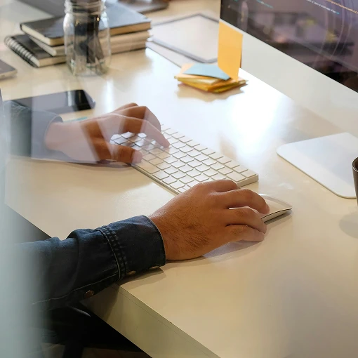 Close-up of man's hands typing on keyboard and using mouse at workstation