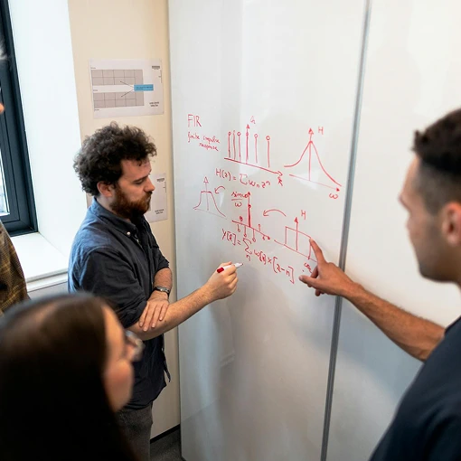 Collaborative analysis session with people discussing formulas and charts on whiteboard