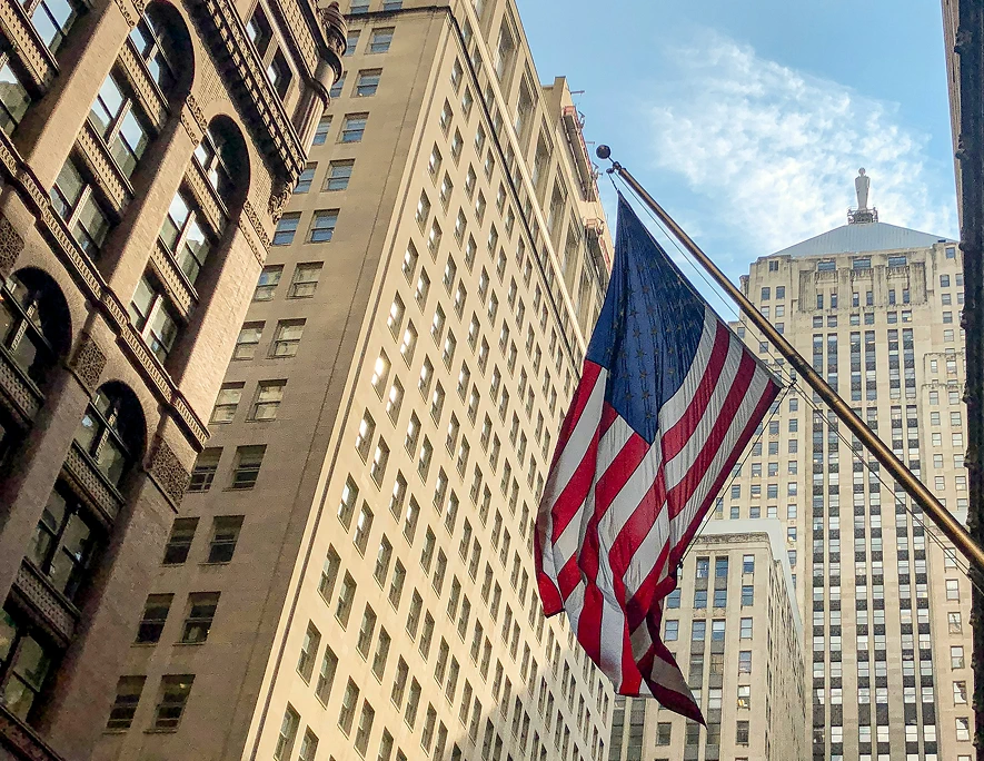 American flag hanging between tall city buildings under a partly cloudy sky