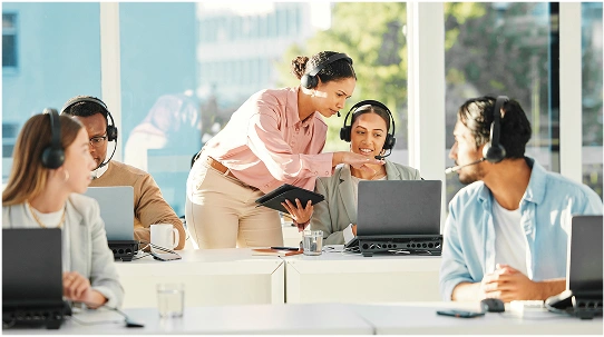 Team of customer support agents wearing headsets at computers, in a brightly lit office.