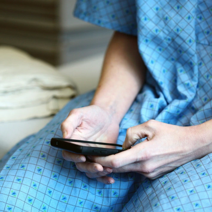 a patient or healthcare provider sitting on a bed looking at a phone