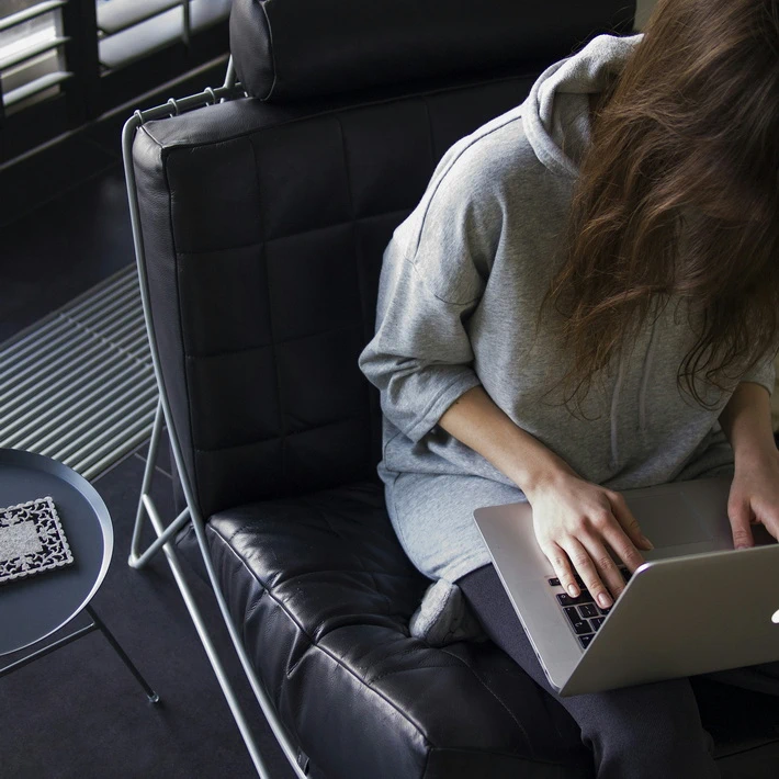 a female quality assurance expert working on a Macbook, sitting in an expensive chair with one leg tucked under her