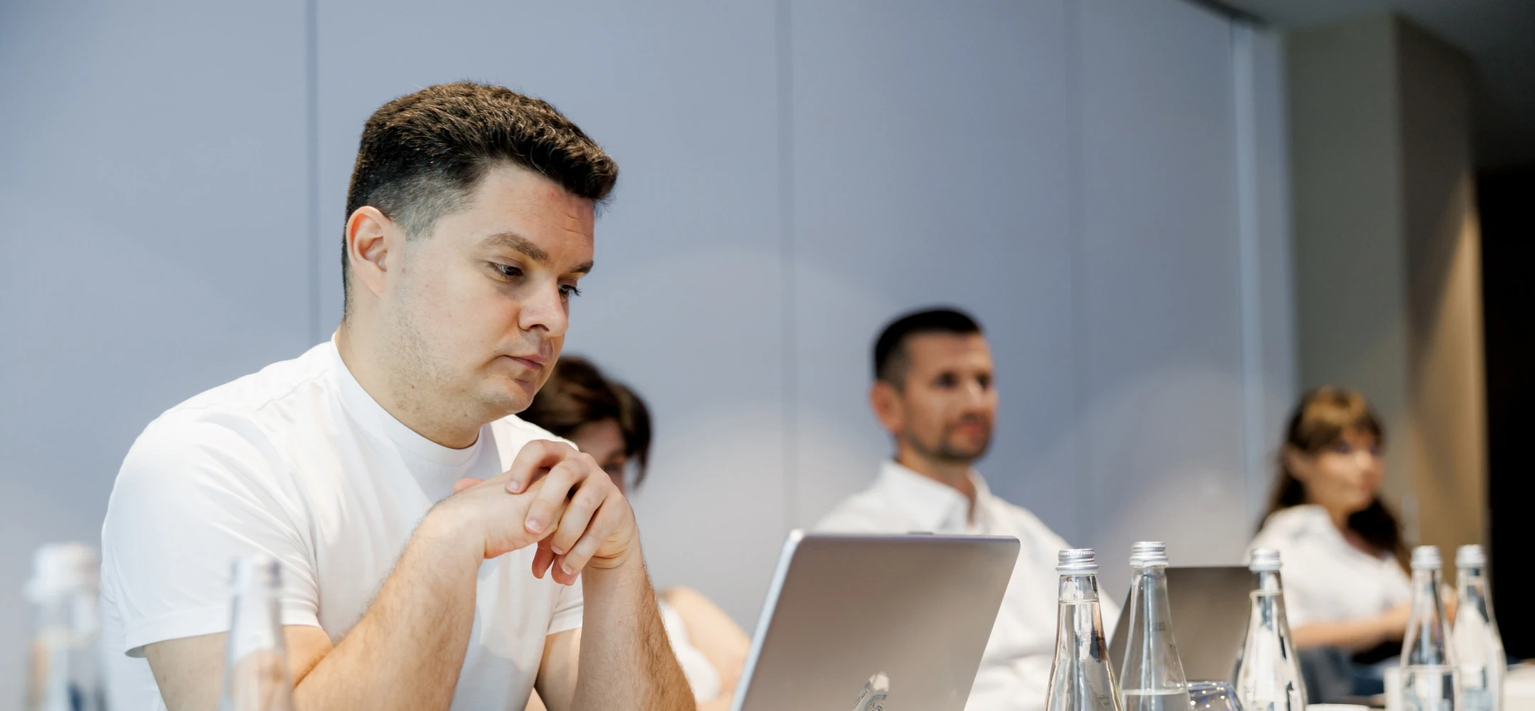 Our amazing tech experts sitting in front of laptops. Working on something cool. There are bottles of water on the table.