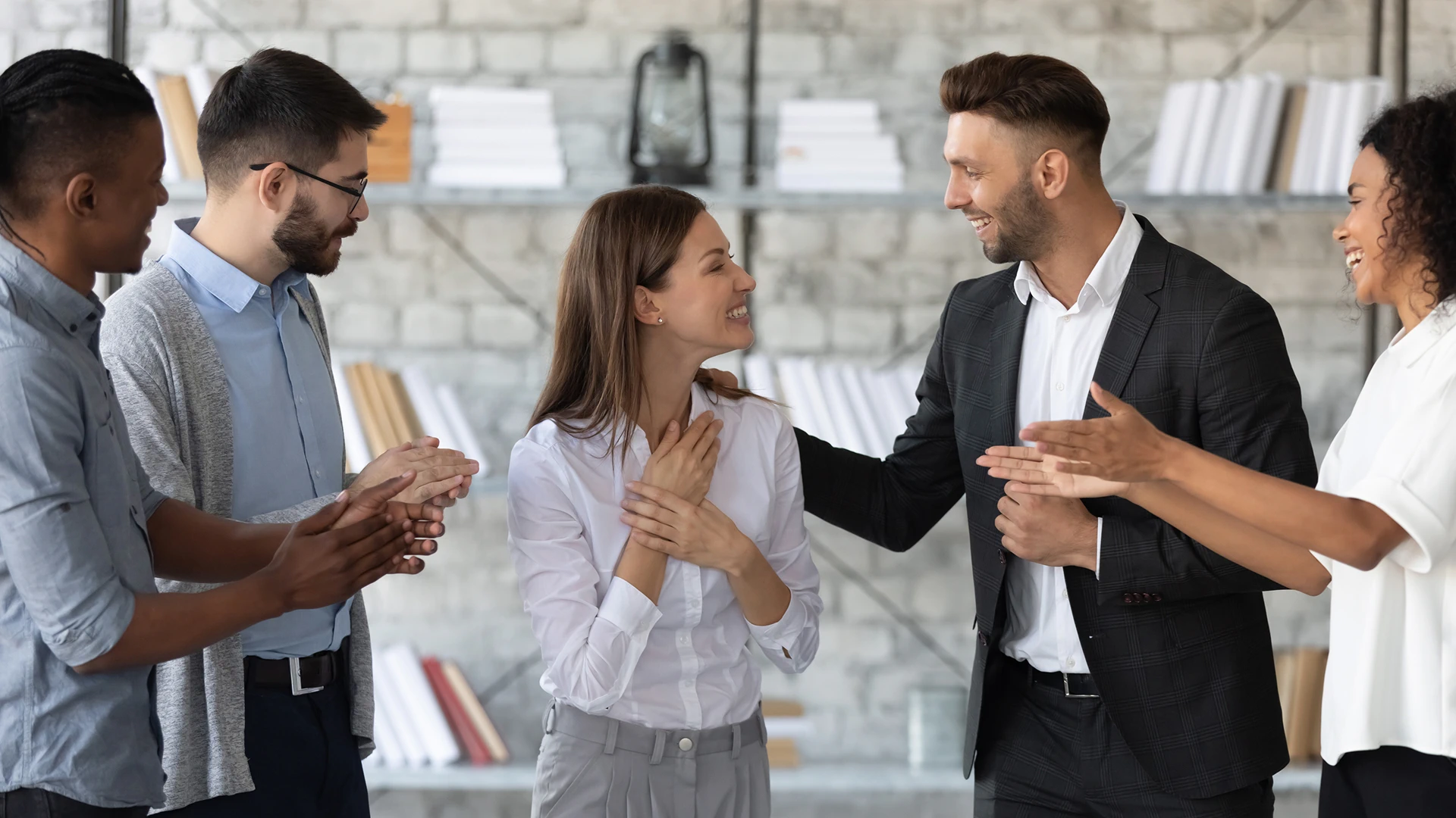 A woman in a white blouse is being celebrated by a group of her colleagues in an office setting