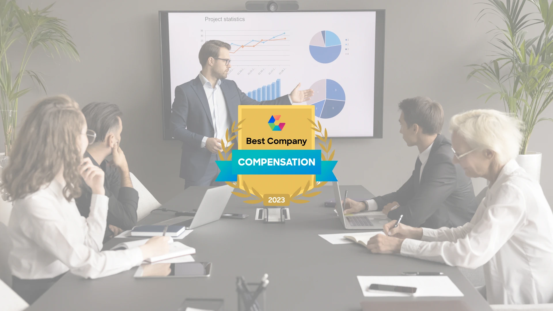 A man in a suit is presenting data from a large screen showing charts and graphs during a professional business meeting