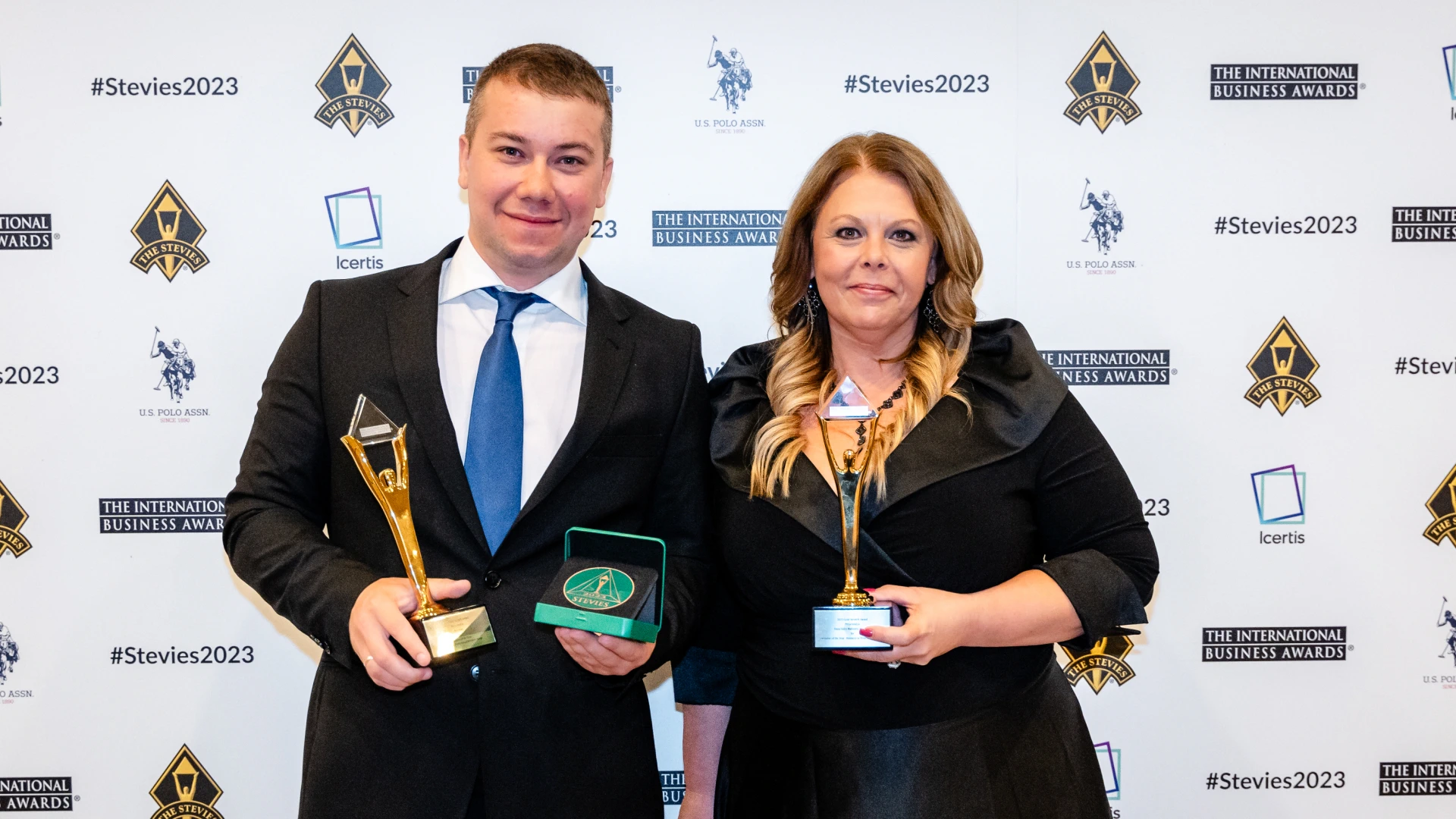 Alexander Tereshchenko, COO, and Dana Sides-Mahoney, Sr. Vice President of Global Operations, wearing business suits, hold awards in their hands with a banner in the background