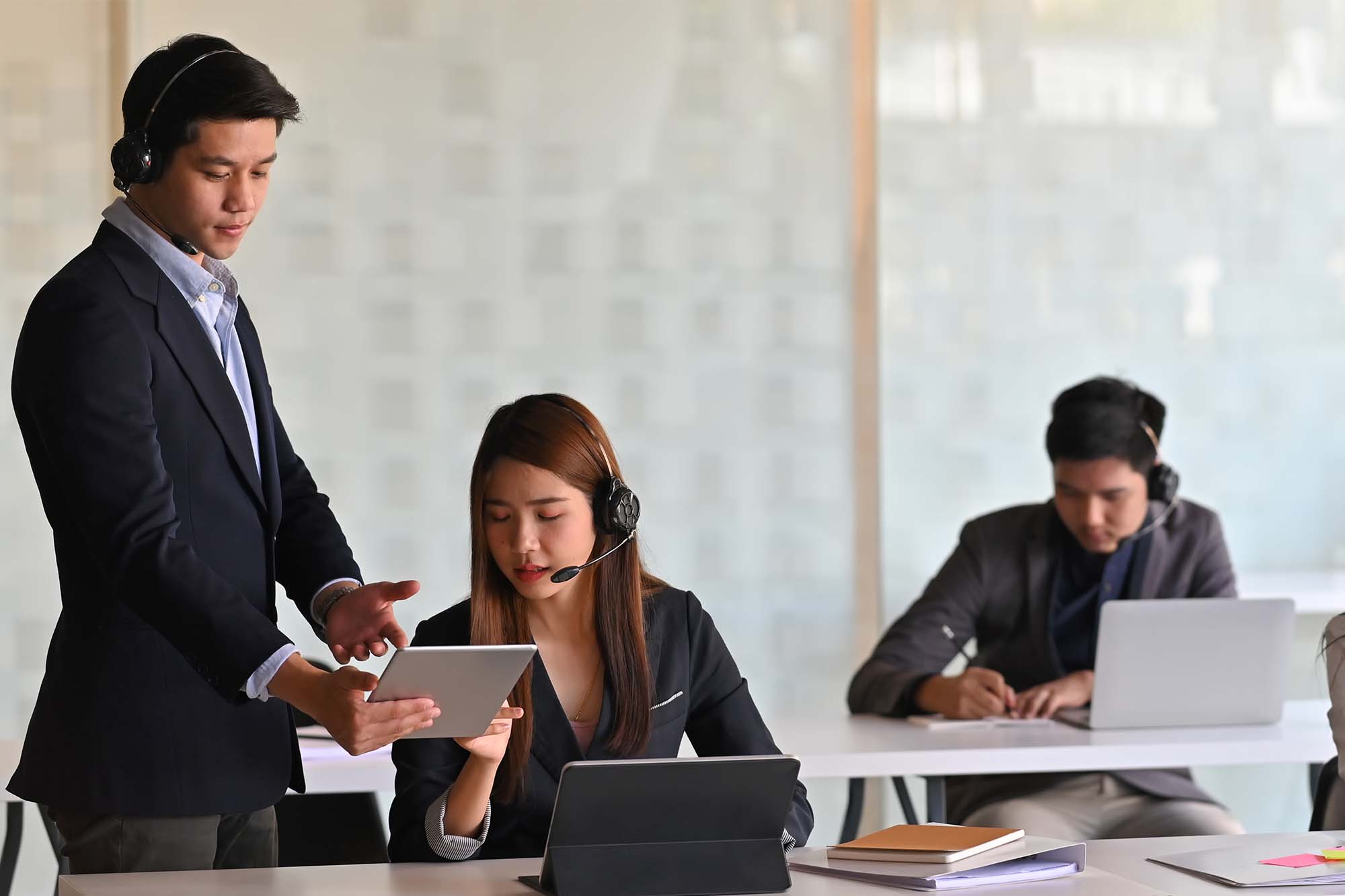 Call center representatives working in an open-space office, wearing suits and headsets.