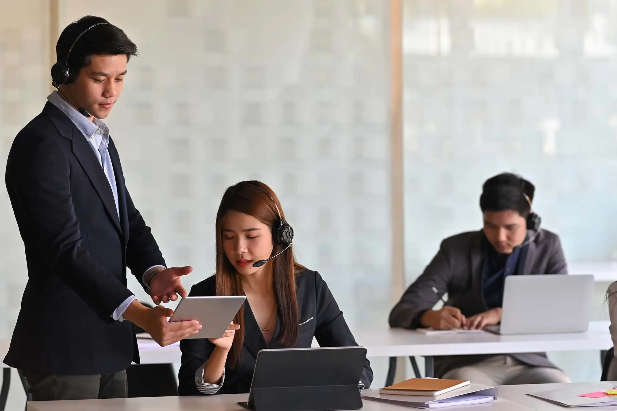 Call center representatives working in an open-space office, wearing suits and headsets.