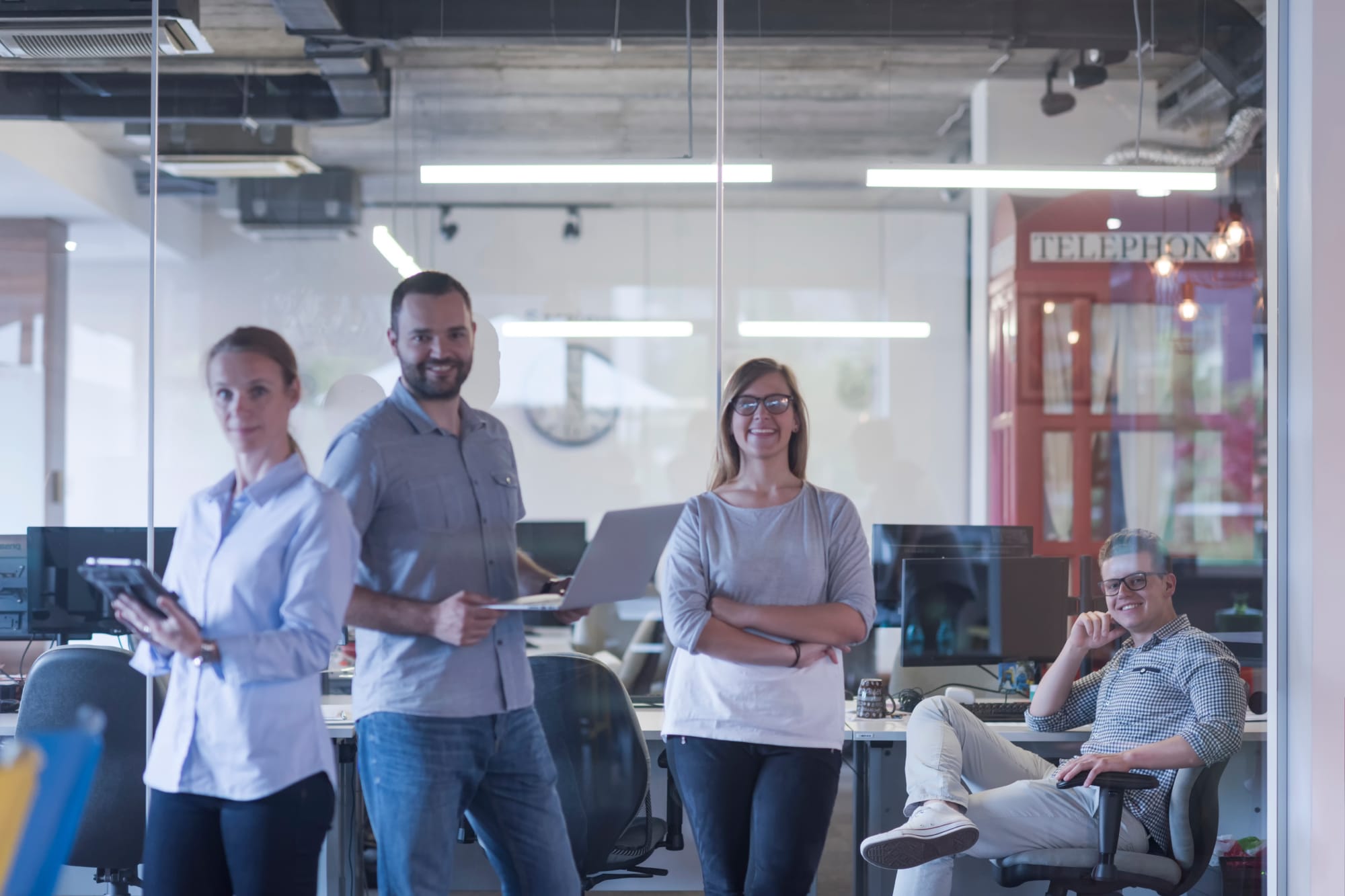 Group of people smiles in a brightly lit, modern office space with glass walls
