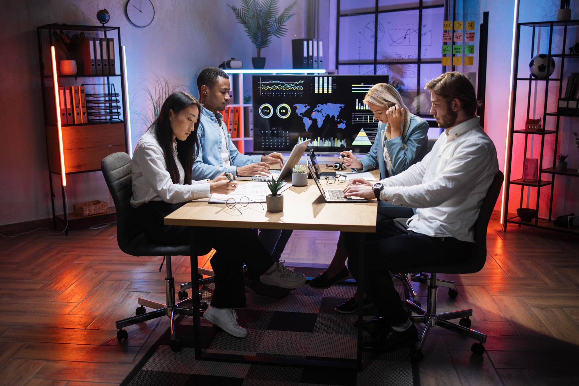 A team of professionals are working at a table with laptops and notebooks.