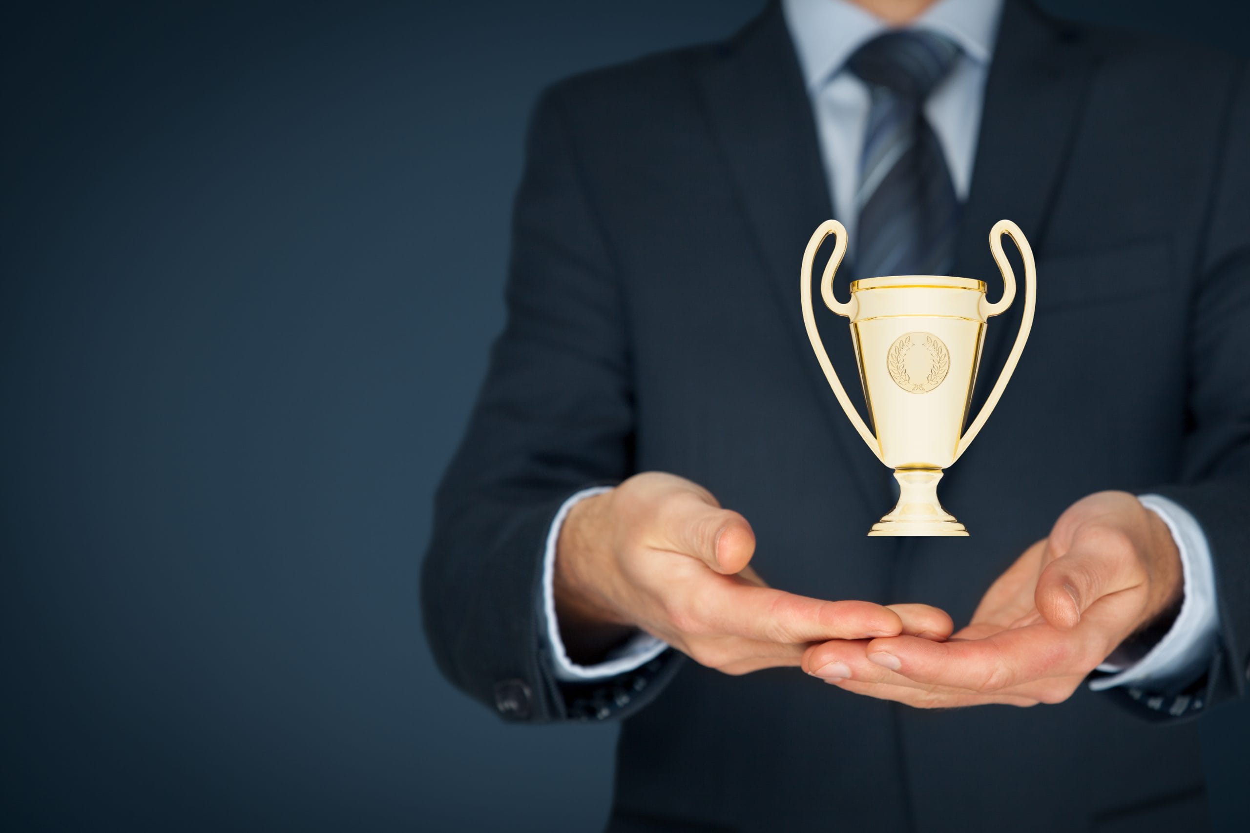 A person wearing a suit is holding a gold trophy